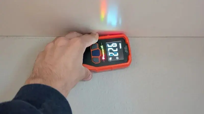 Hand holding a pinless moisture meter against a wall to check for hidden water in a West Chester home