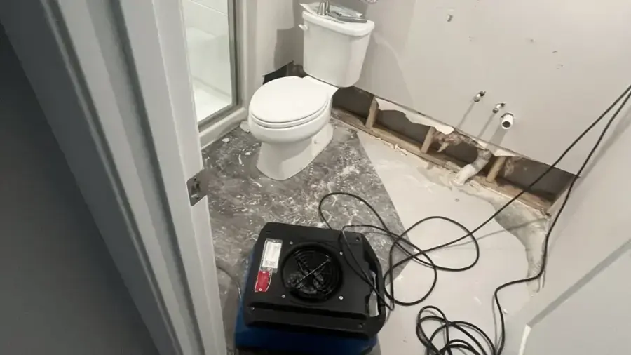Bathroom with the lower drywall removed and an air mover drying the wall cavity