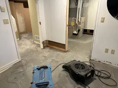 Air movers and a dehumidifier drying a bare subfloor beside opened walls in a West Chester home