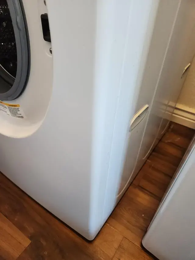 Water pooled on a wood floor beside a leaking washing machine