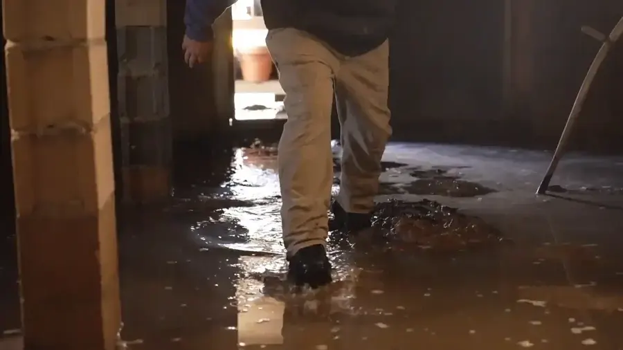 Person in work boots wading through a flooded basement with wet stud walls