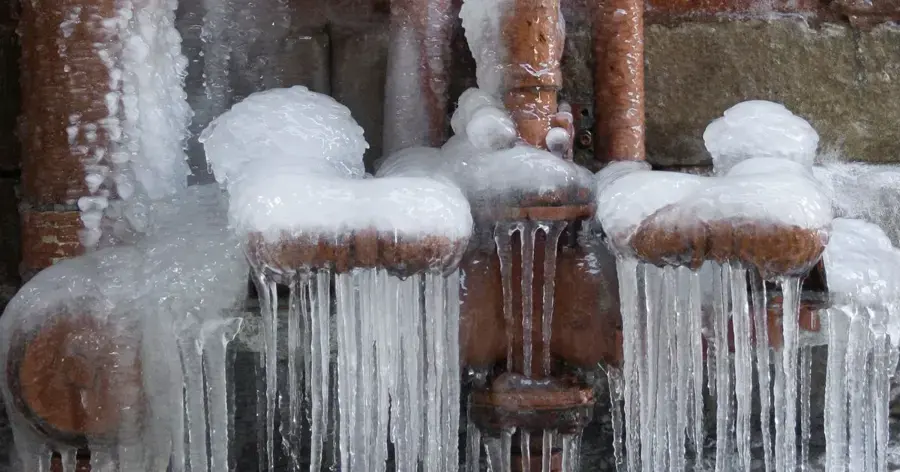Copper pipes and fittings coated in ice and icicles during a hard freeze