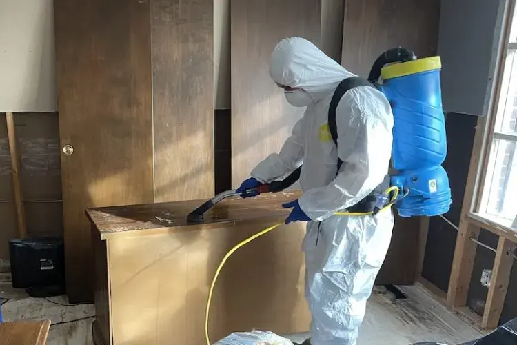 Technician in a full protective suit spraying antimicrobial on cabinets after a sewage backup