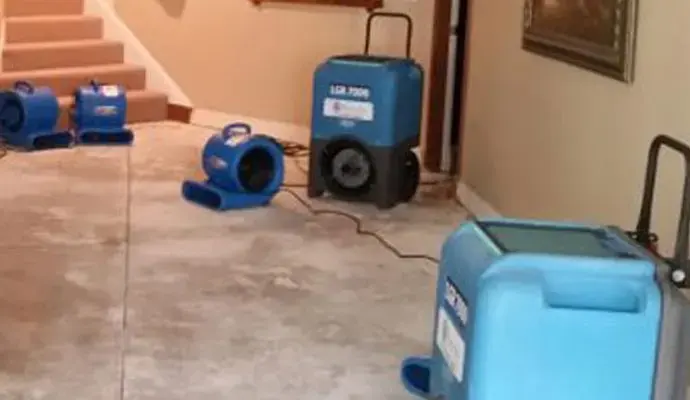 Air movers and a dehumidifier drying a floor at the foot of a staircase