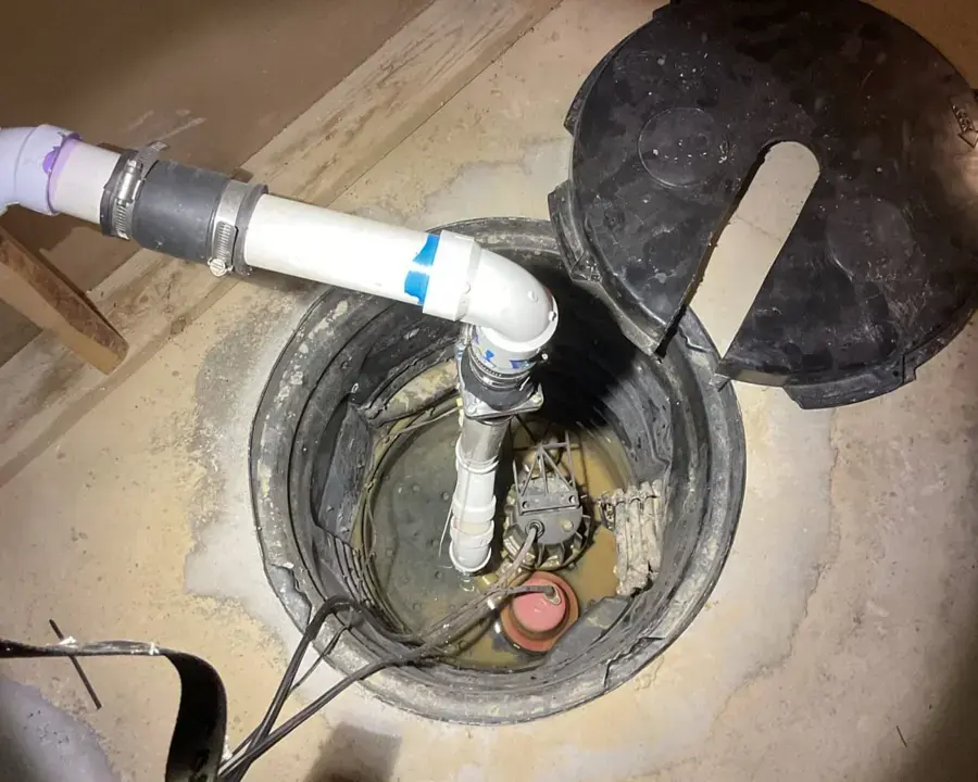 Open sump pit with the pump, check valve and discharge pipe in a basement floor